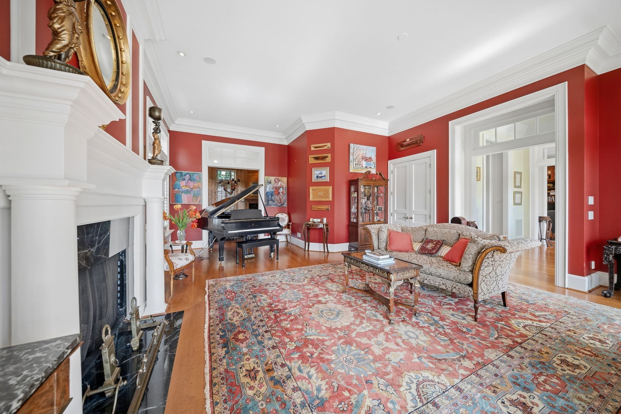 View across the red living room toward an archway leading to adjoining yellow-walled rooms, with a grand piano in the corner.