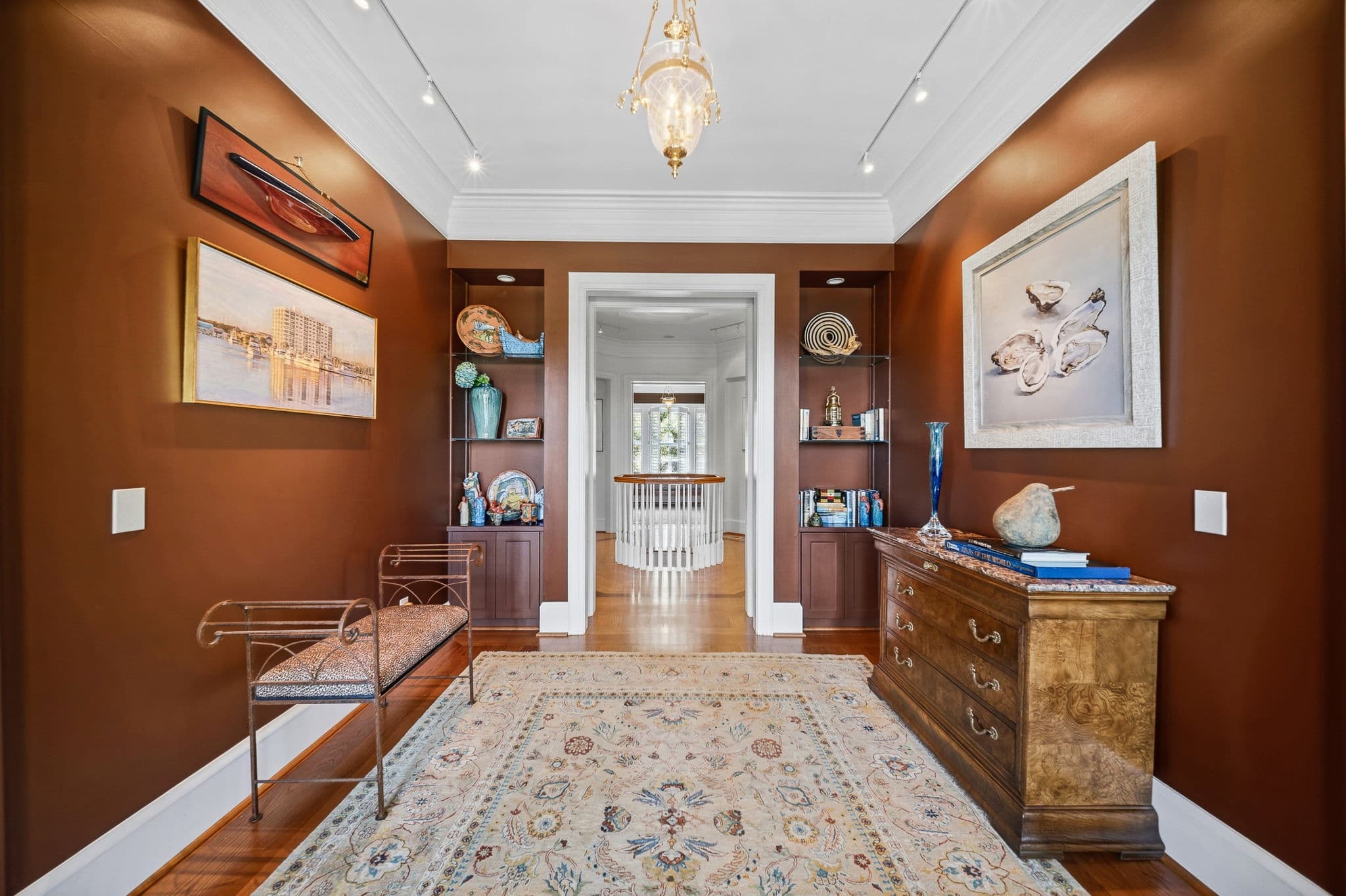 Hallway with built-in display shelves, coastal artwork, and a view toward the staircase.