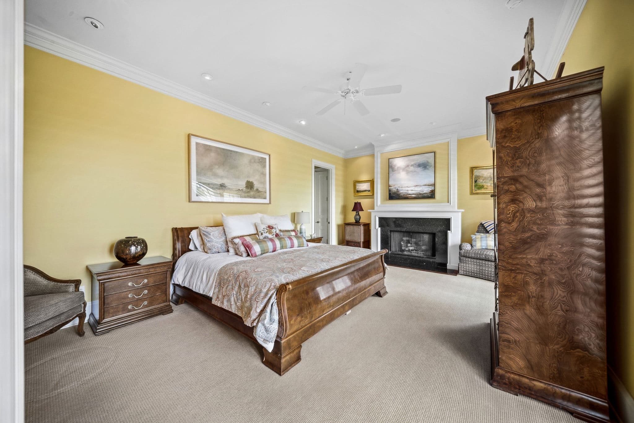 Yellow bedroom with a wood sleigh bed, a black marble fireplace, and a burl-wood armoire.