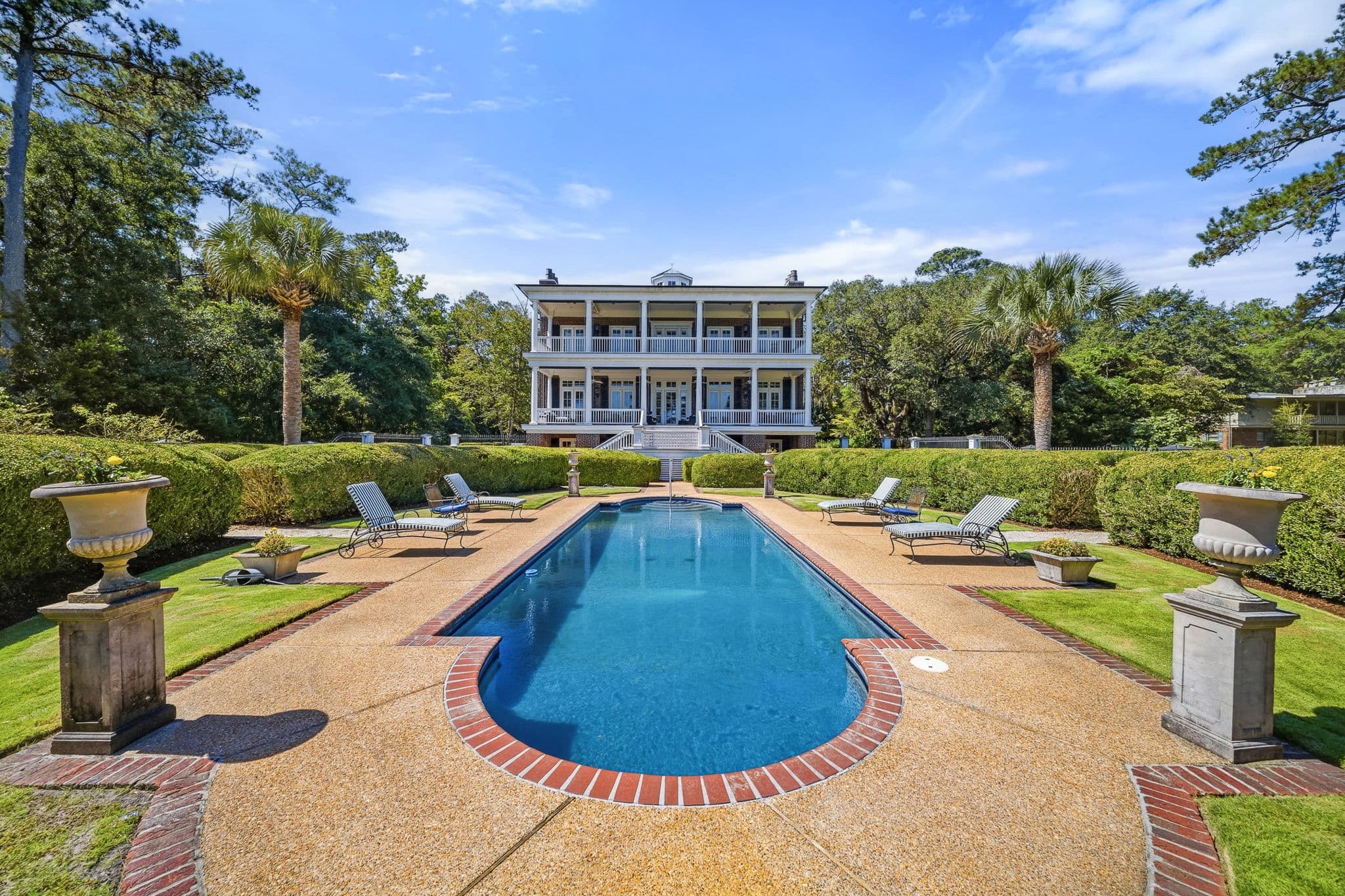 Rectangular pool with stone urns on pedestals and a multi-story house in the background.