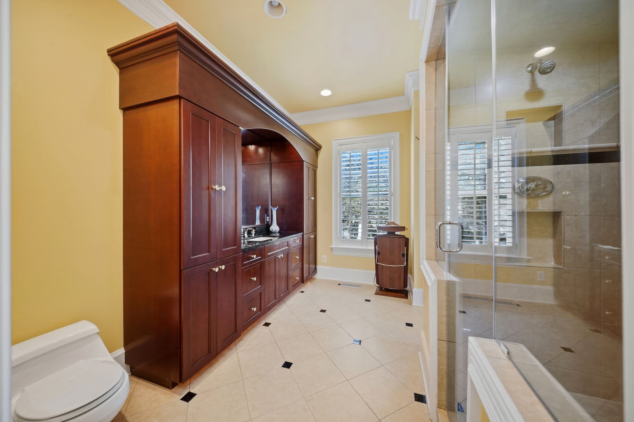 Bathroom with tall dark wood cabinetry, a tile floor with diamond inlays, and a glass-walled shower in the background.