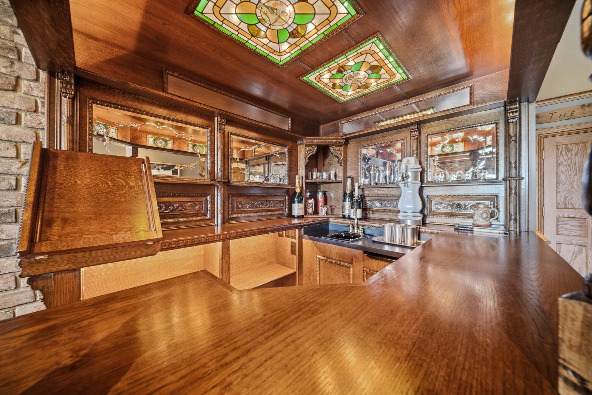 Interior of a wood bar with mirrored back panels, stained glass ceiling inserts, and glassware.