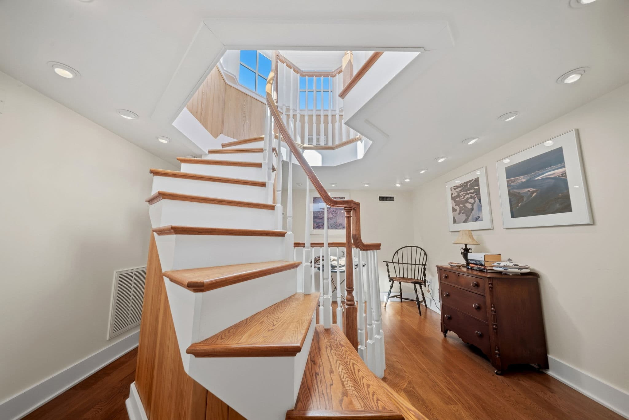 Wood staircase with white balusters switching back beneath a skylight window, with a dresser and chair at the landing.