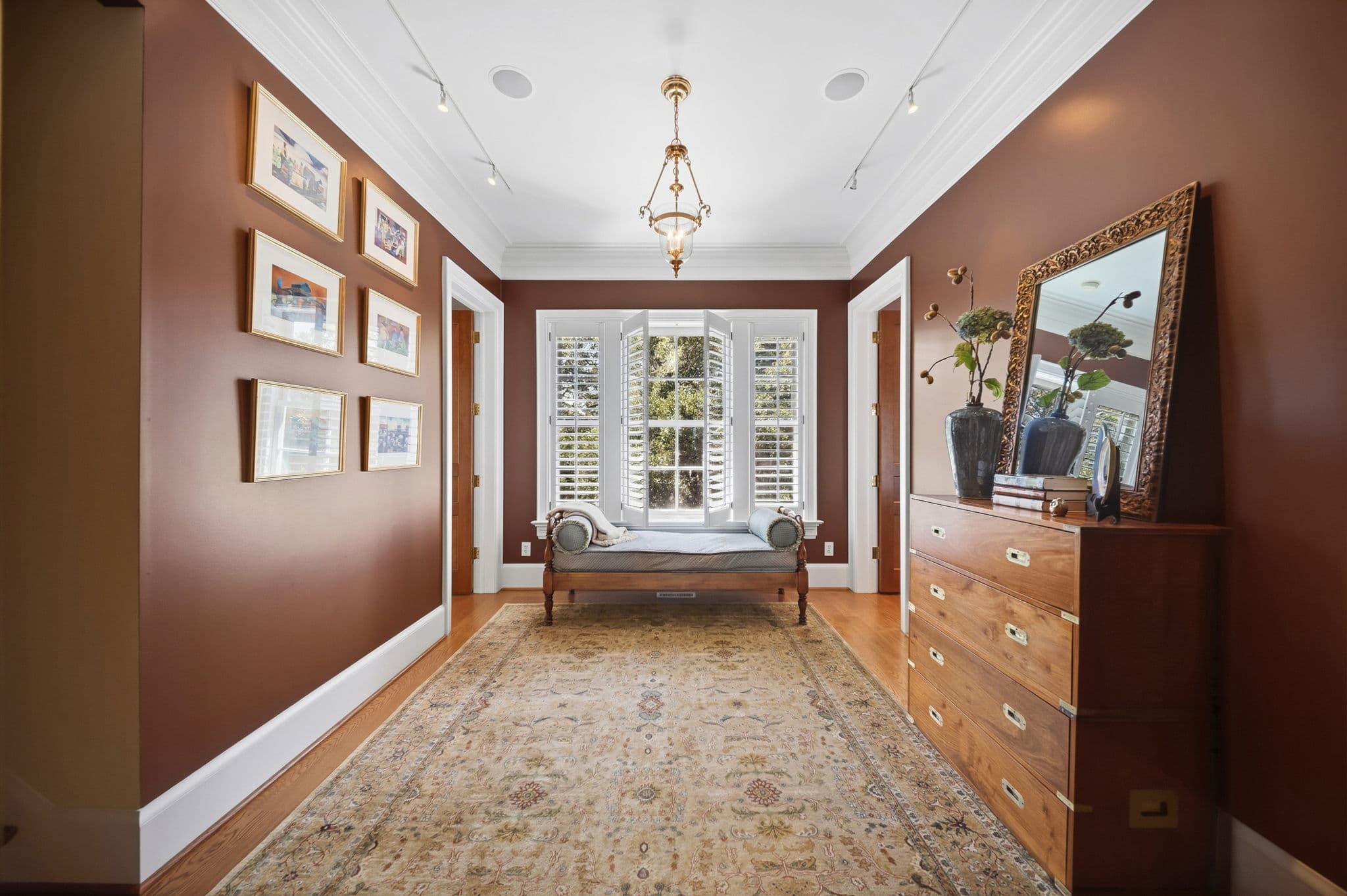 Hallway with terracotta walls, a grid of small framed artwork, and a window seat with bolster pillows.