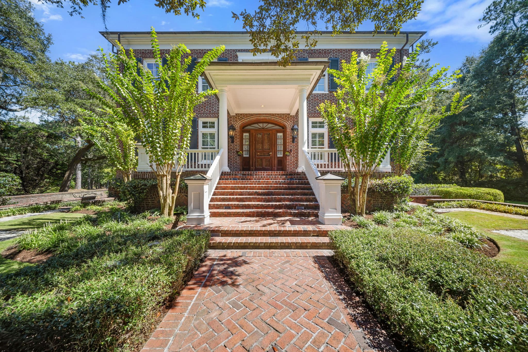 Two-story white portico with tall columns over a brick front entrance with an arched wood door and brick steps.