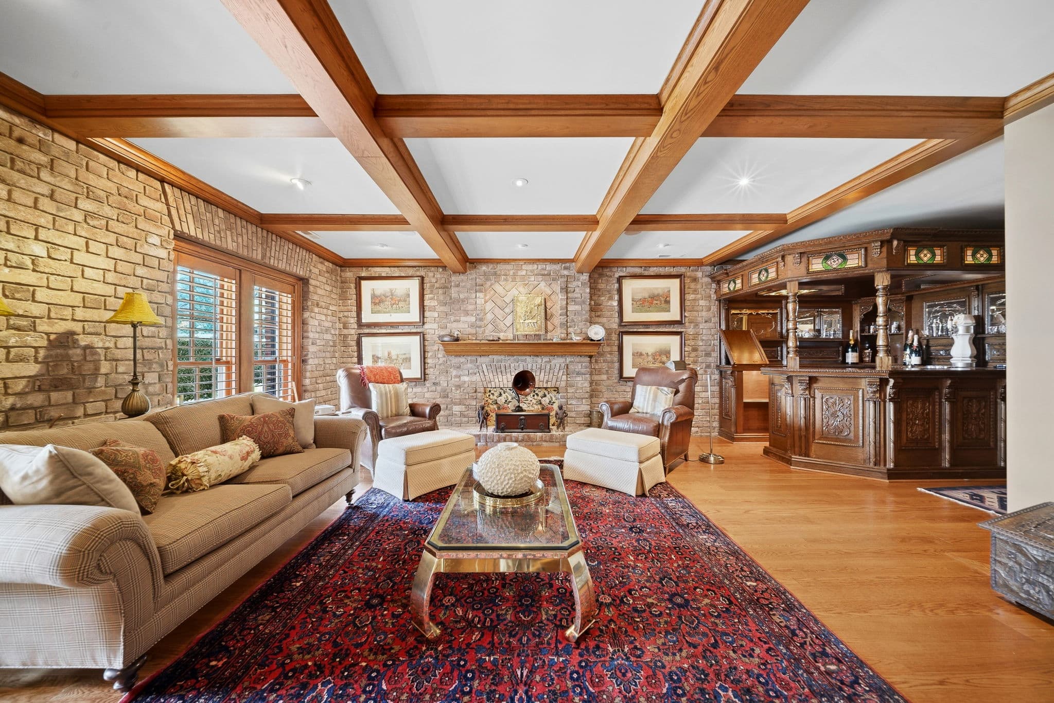 Living area with plaid sofa, ottomans, brick fireplace, and a carved wood bar in the background.