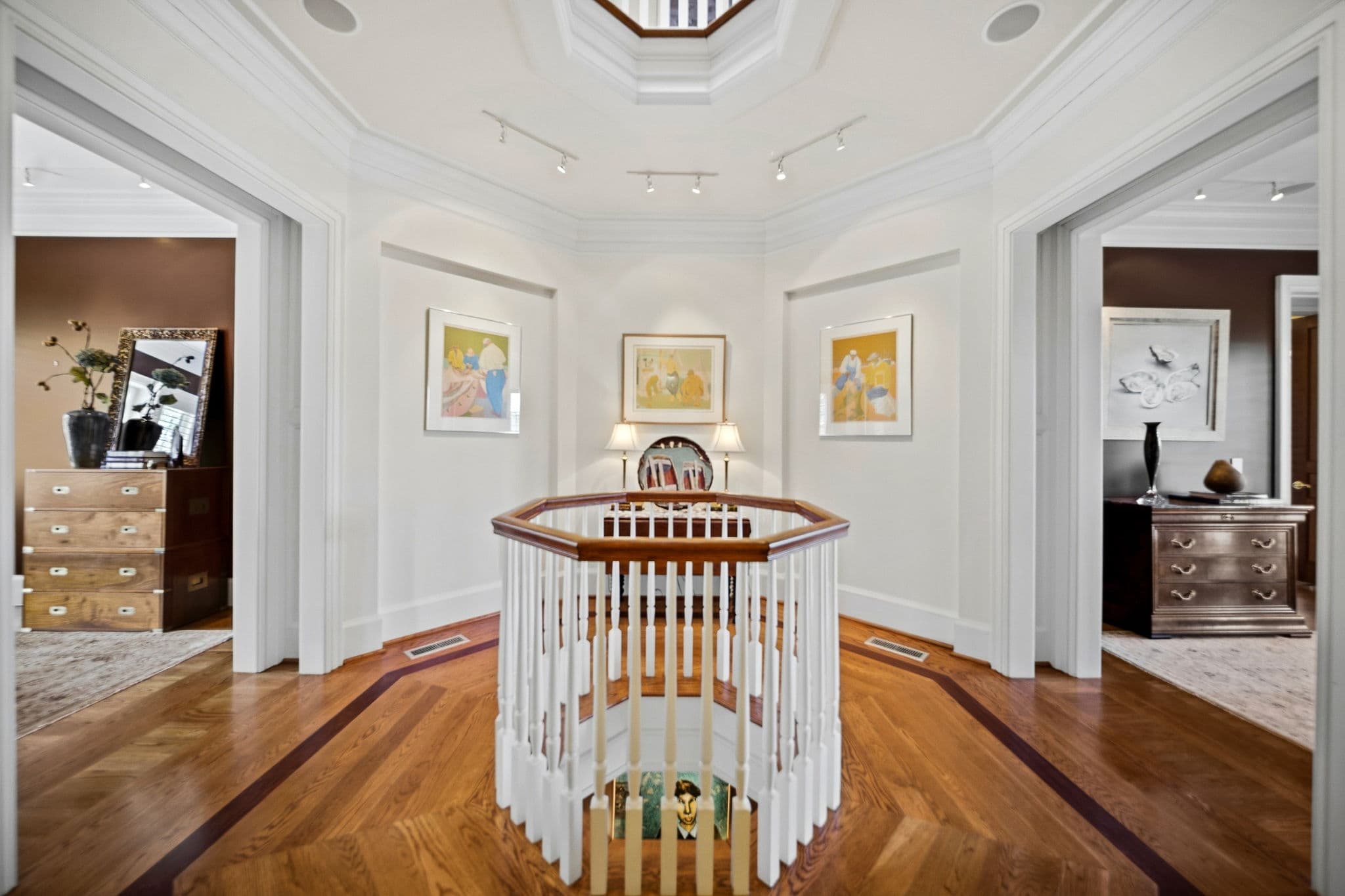 Upper landing with a campaign-style chest and dresser on either side and a round table inside the stair railing.