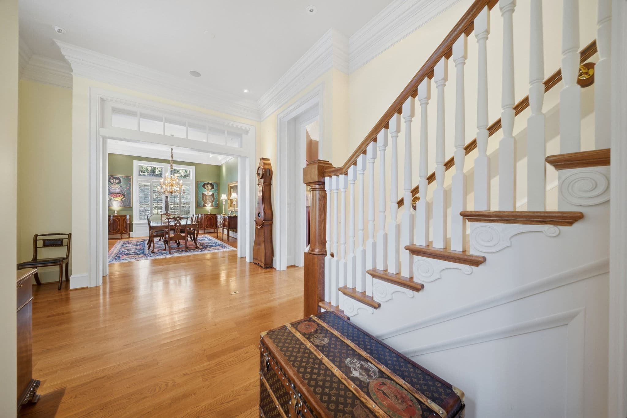 View from a staircase down to the entry hall and dining room, with a vintage steamer trunk at the base of the stairs.