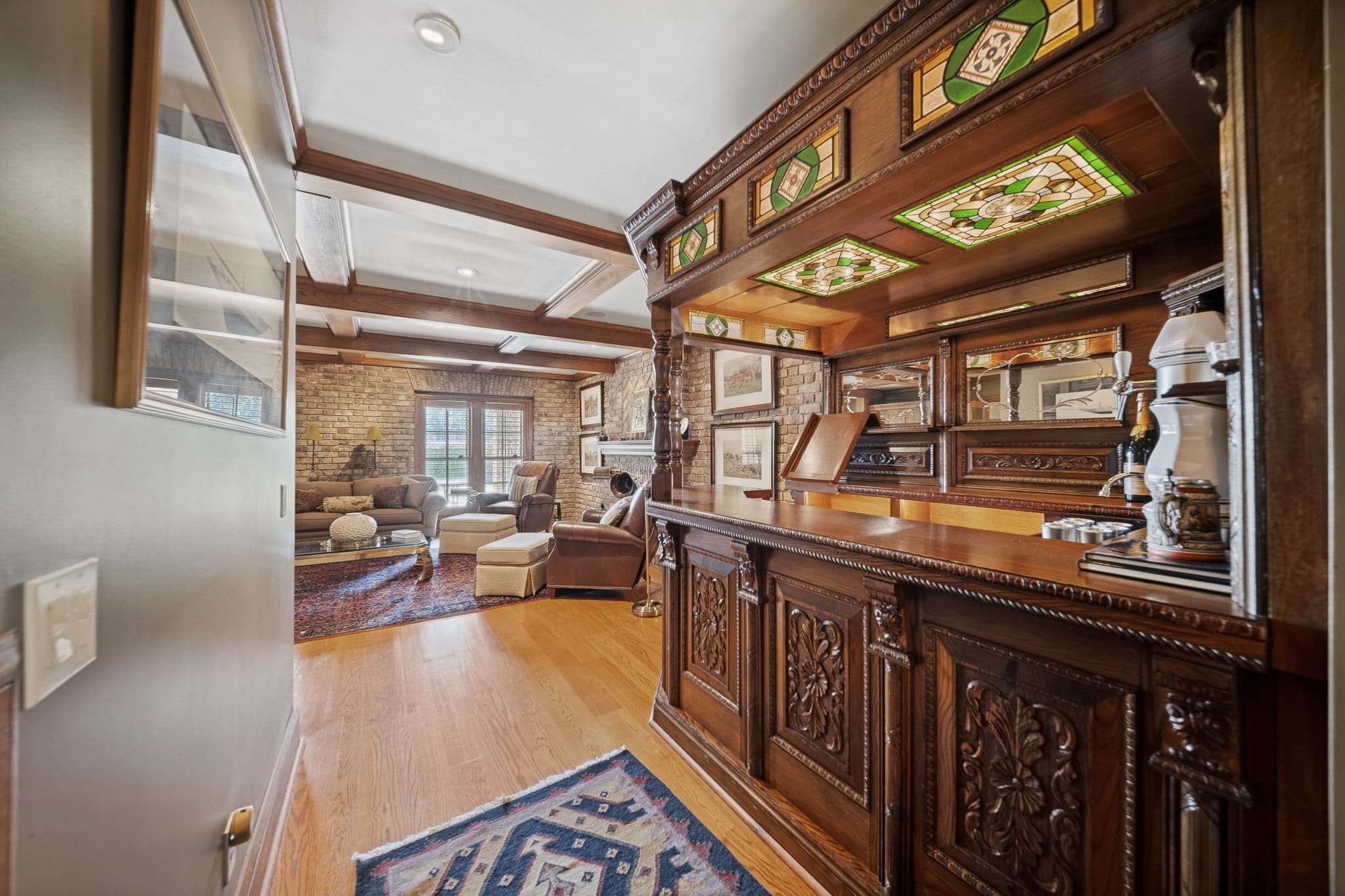 Antique wood bar with green and amber stained glass panels, seen from a hallway with a brick-walled room beyond.