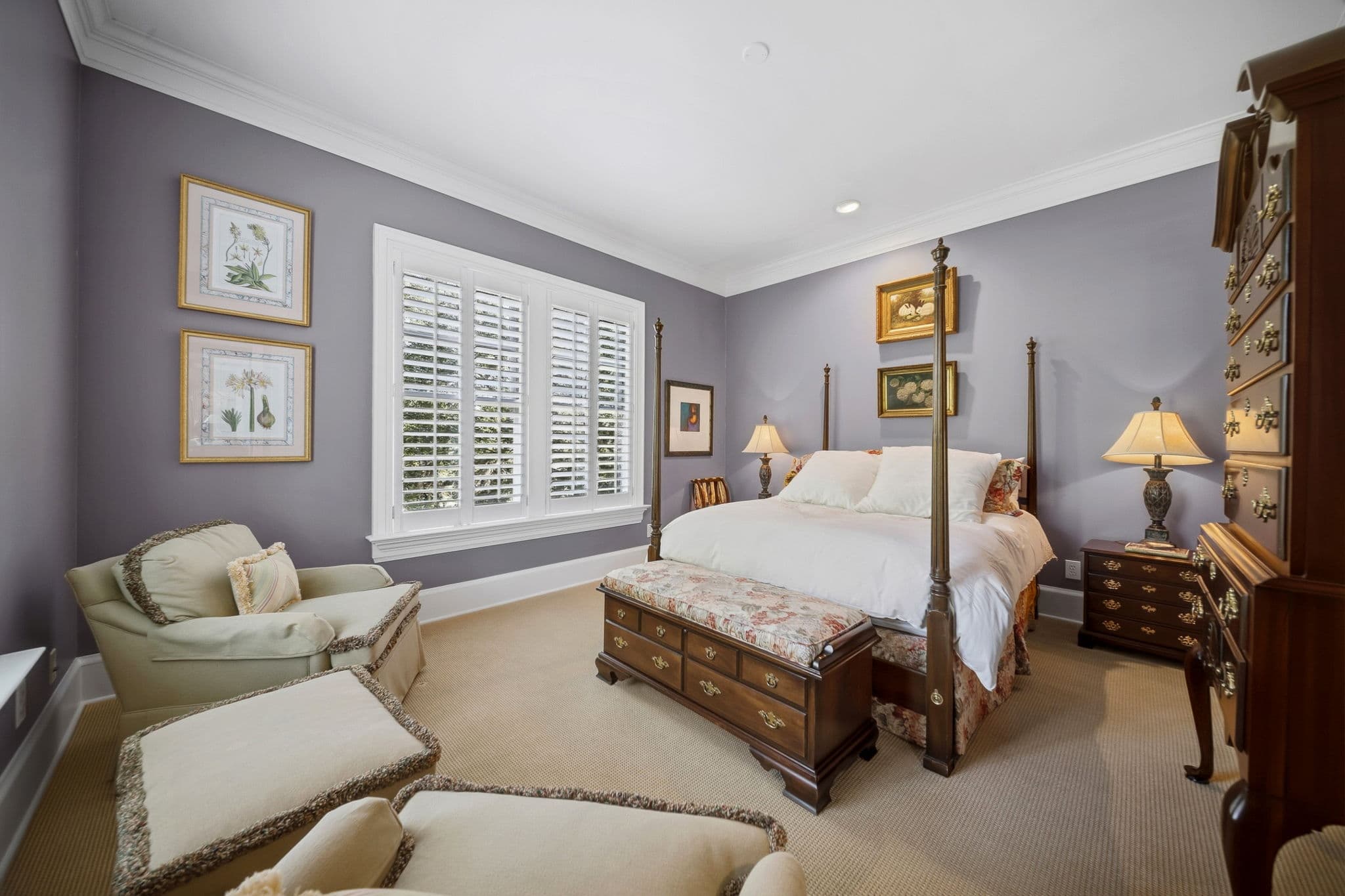 Bedroom with lavender walls, a four-poster bed, botanical artwork, and a wood chest at the foot of the bed.