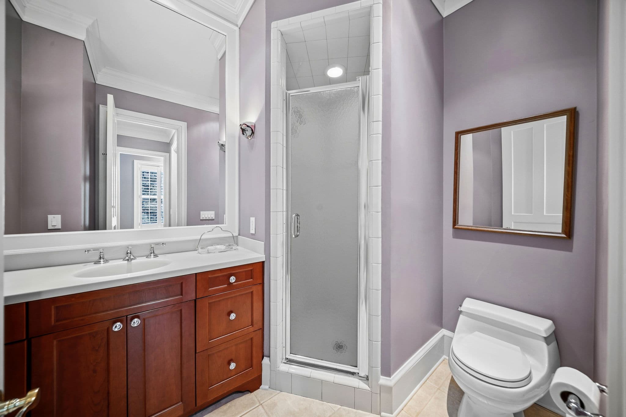 Bathroom with a narrow glass shower enclosure, a toilet, and a small wood-framed mirror on the wall.