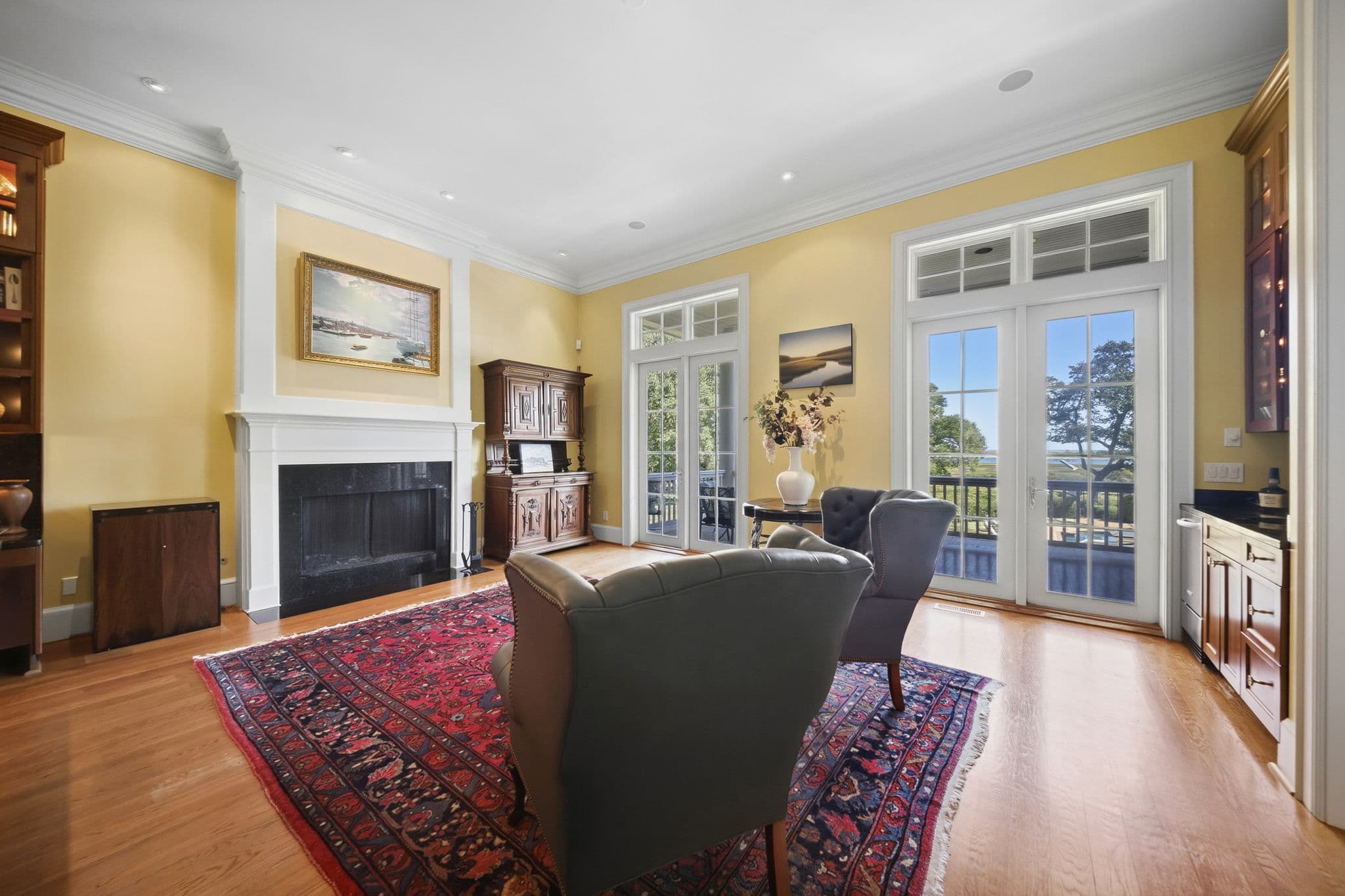 Living area fireplace with framed painting above, and French doors showing a water view.