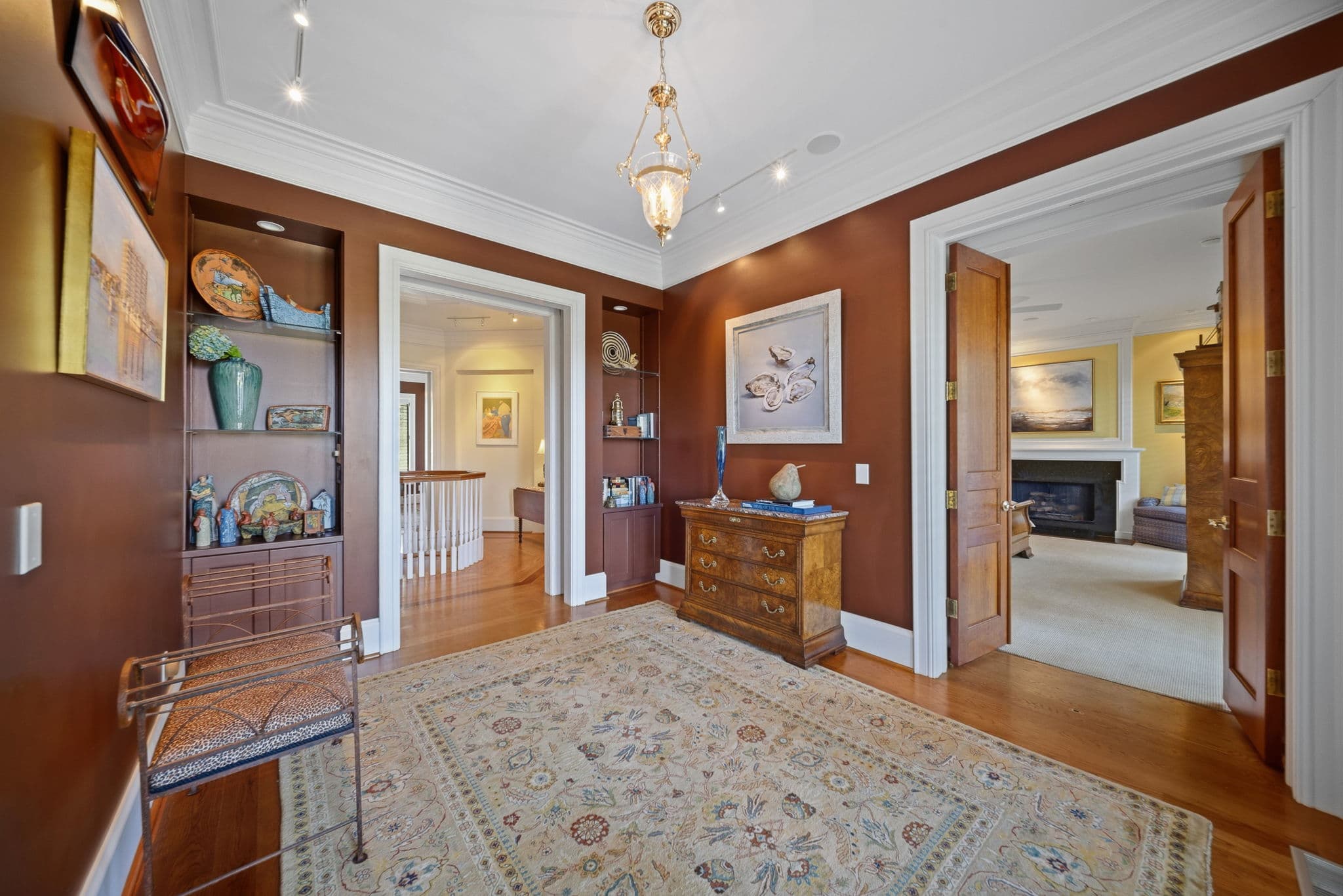 Hallway with terracotta-colored walls and an oyster still-life painting, opening onto another room with a fireplace.