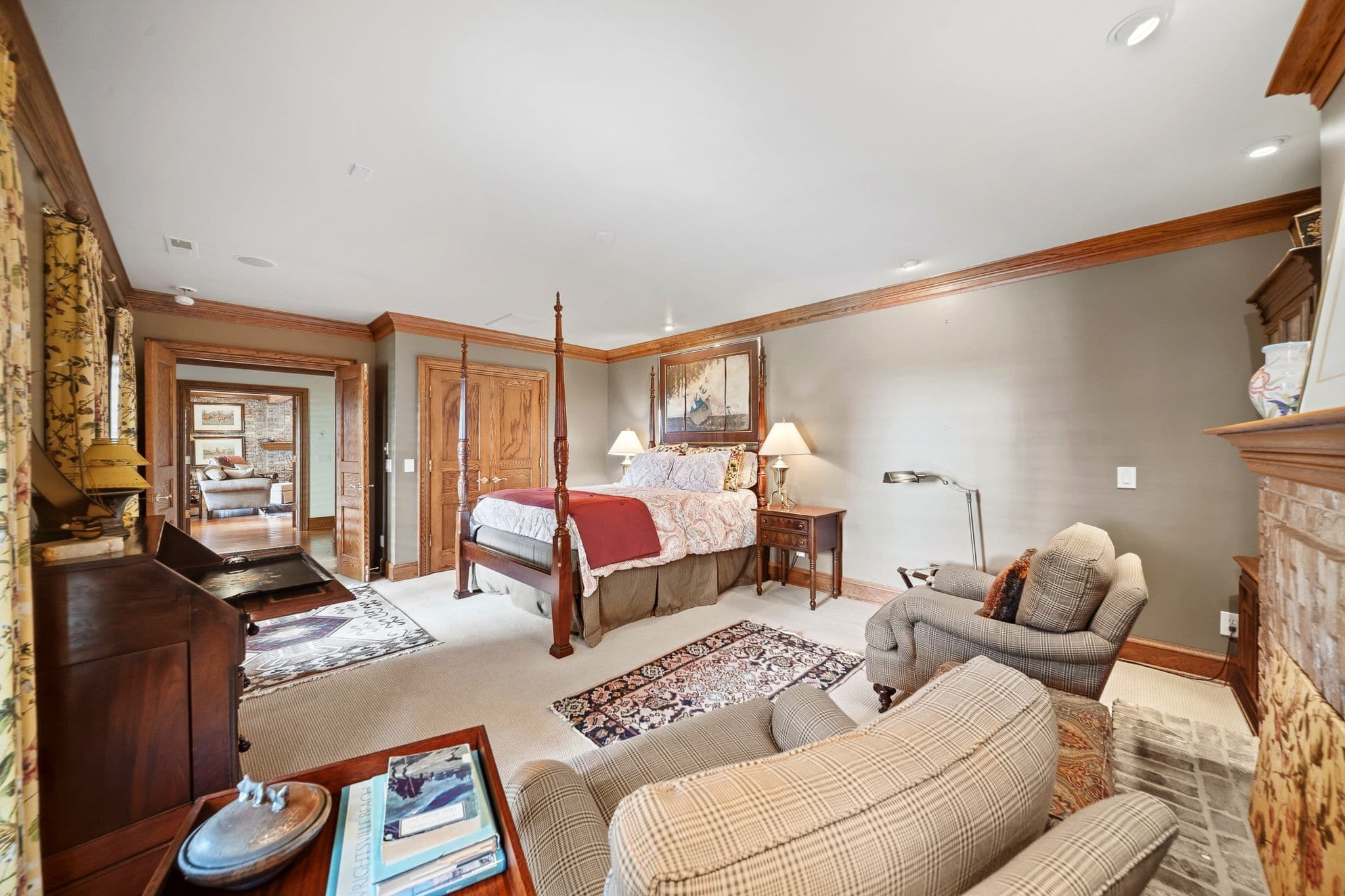 Bedroom with open double doors to an adjoining room, plaid loveseat, and brick fireplace visible.