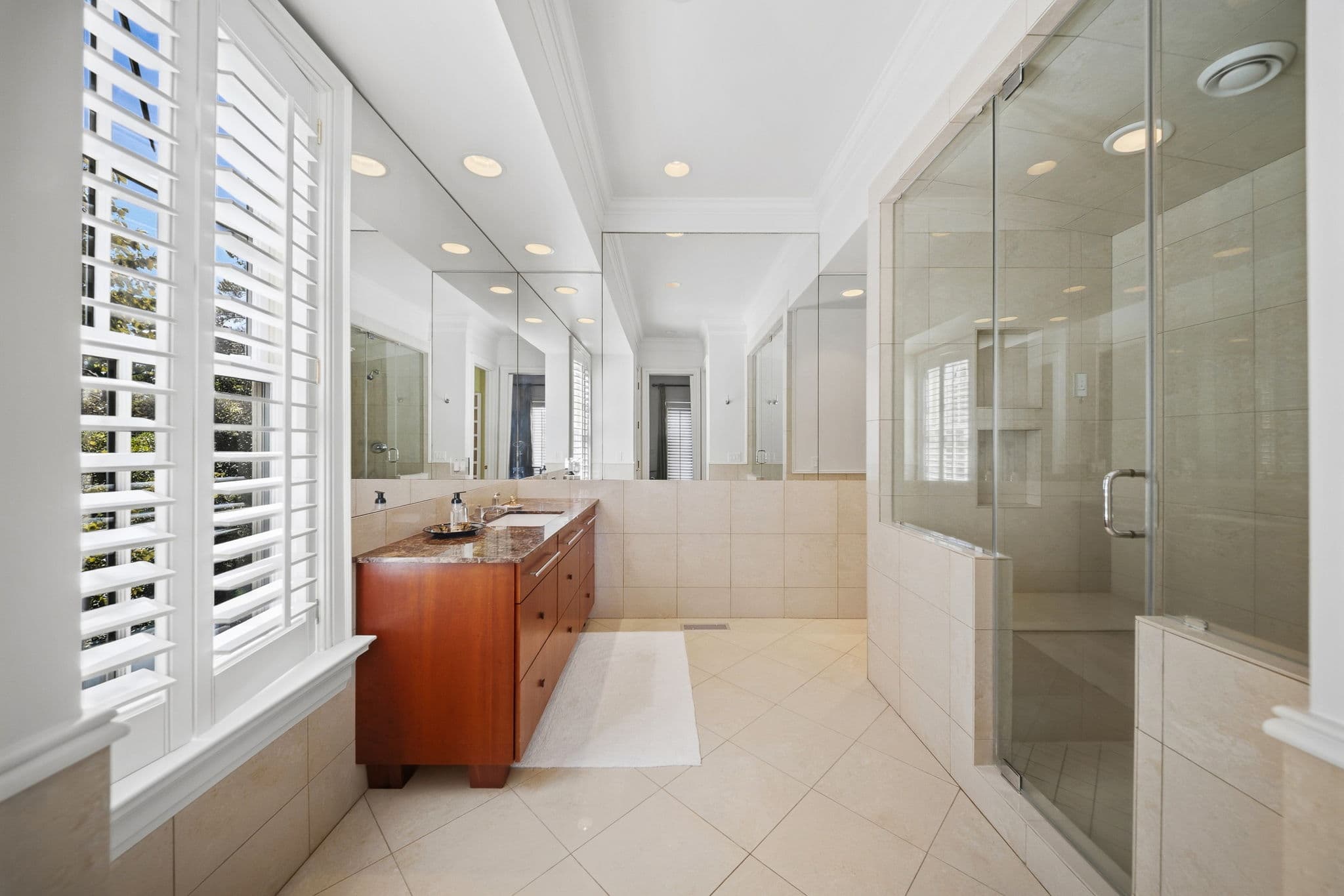 Long bathroom with a mirrored wall, marble-topped vanity, and glass shower enclosure.