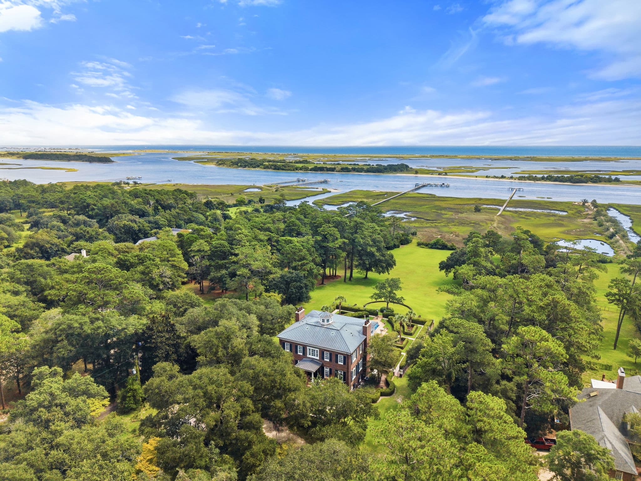 Aerial view showing the house, surrounding trees, and the marsh with docks and waterways beyond.