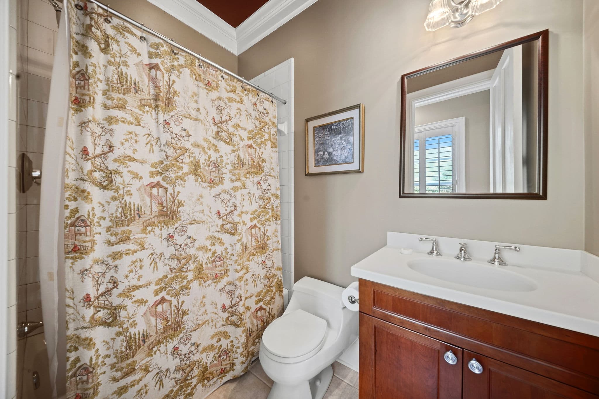 Bathroom with a patterned toile shower curtain, a wood-framed mirror, and a cherry vanity.