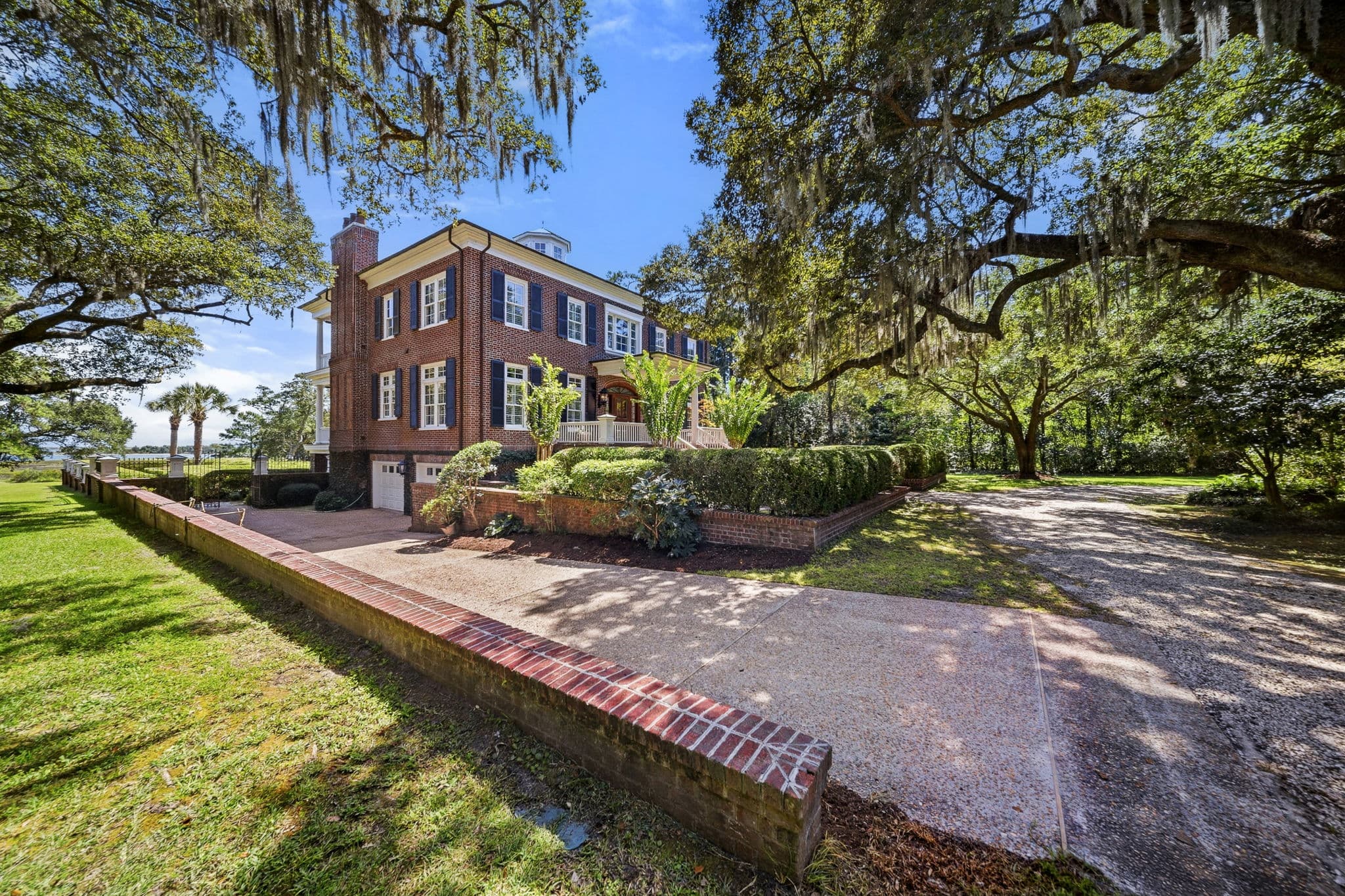Driveway beside a brick retaining wall with a second-floor balcony and landscaped foundation plantings.