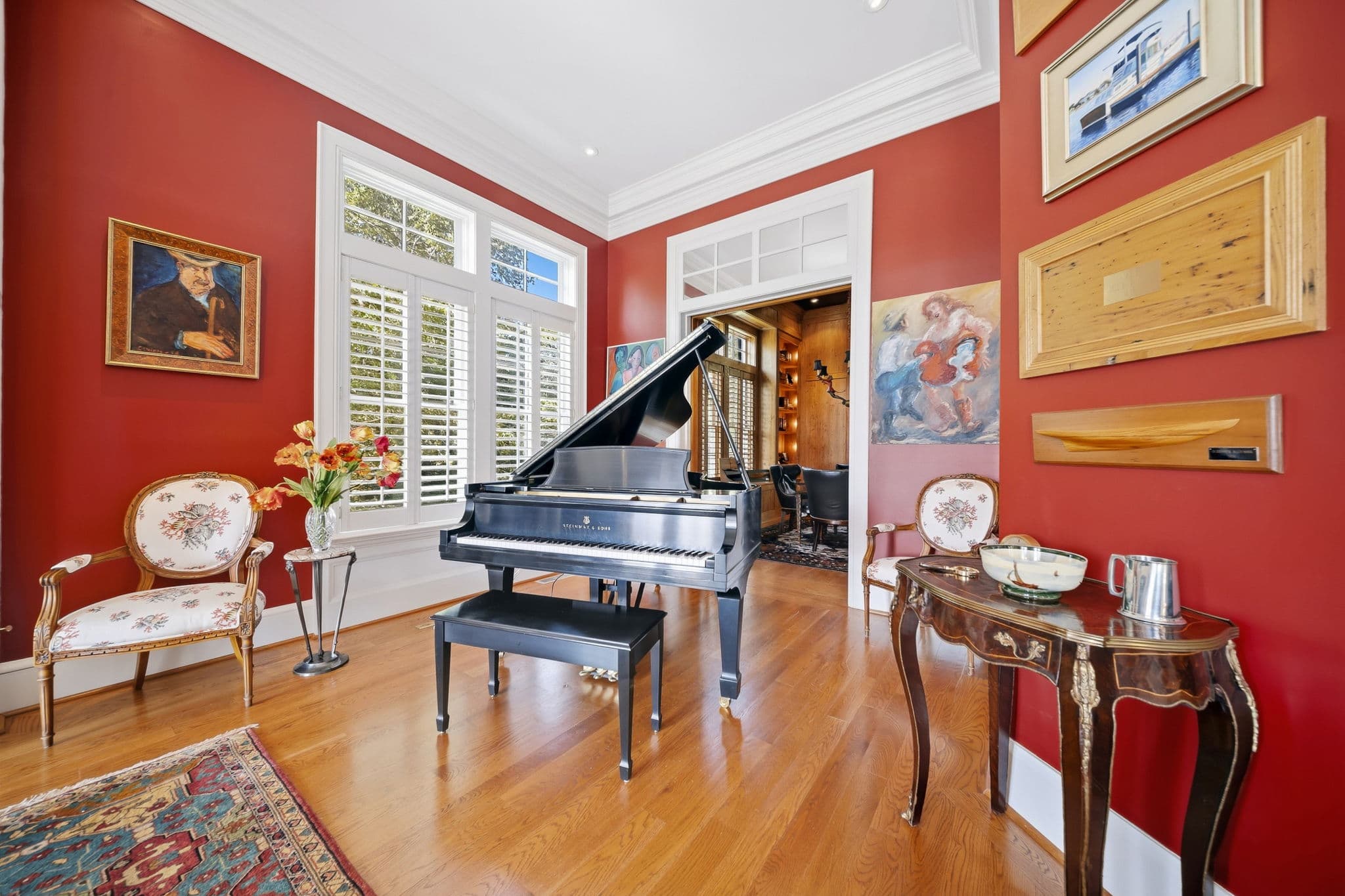 Grand piano with visible Steinway & Sons nameplate, beneath a vaulted red ceiling, with a doorway to a wood-paneled study beyond.