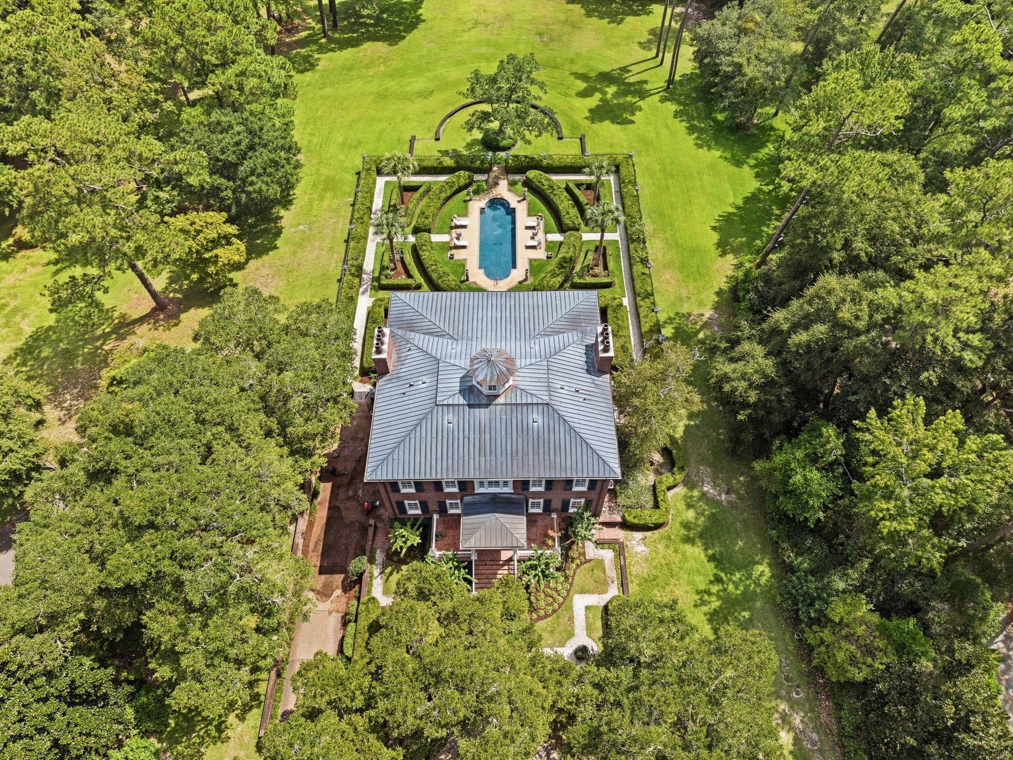 Overhead aerial view of the house's metal roof and cupola above a symmetrical hedge garden and pool.