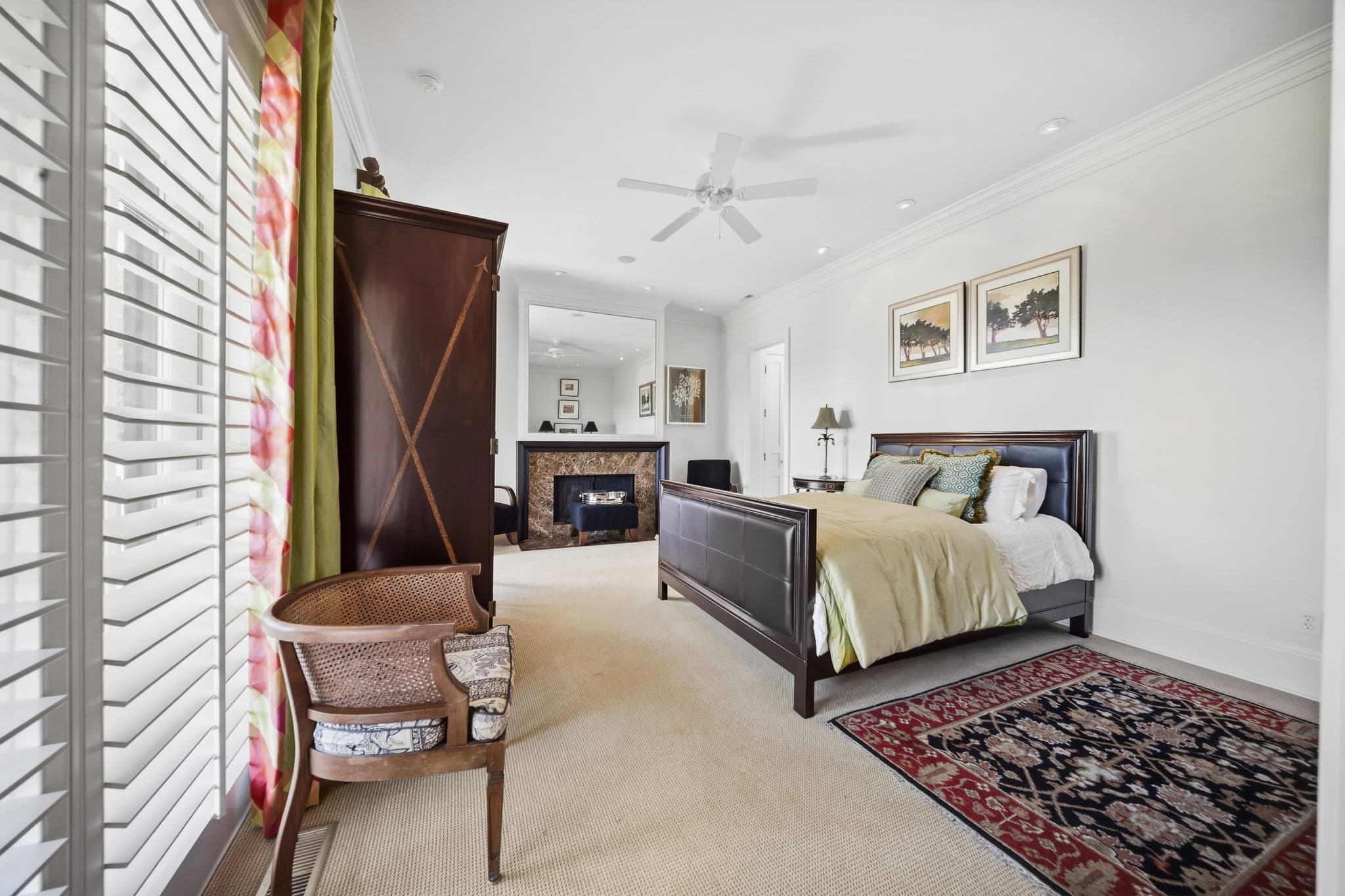 Bedroom with a leather-headboard bed, a marble fireplace and mirror, and an inlaid wood armoire.