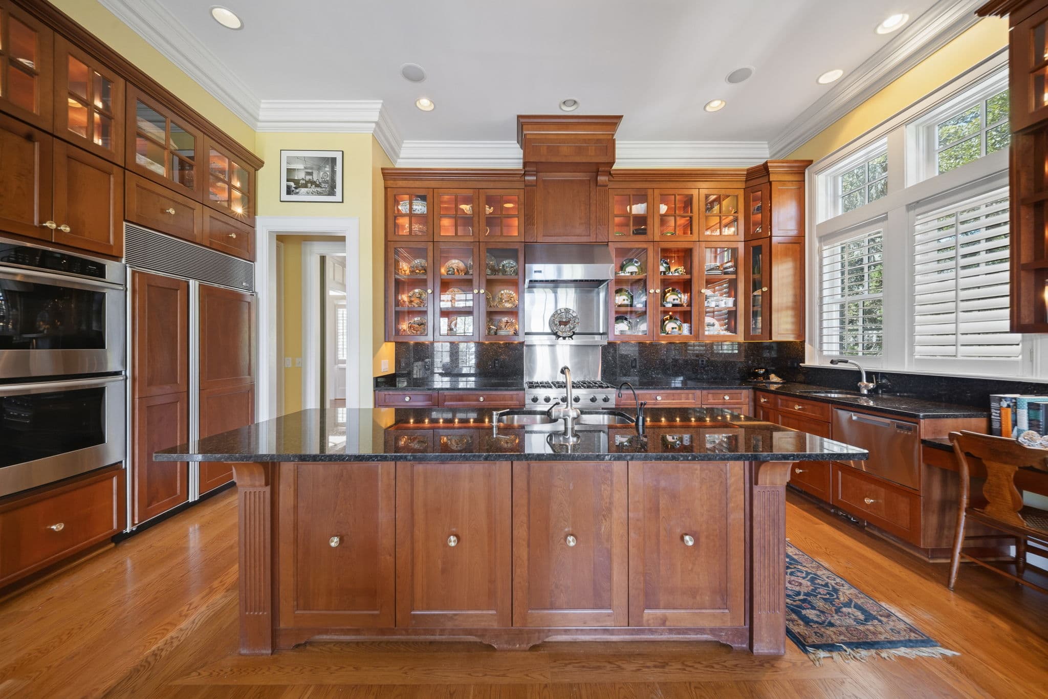 Kitchen island with two undermount sinks and a gas cooktop, plantation shutters on the window behind, and a built-in bookshelf.