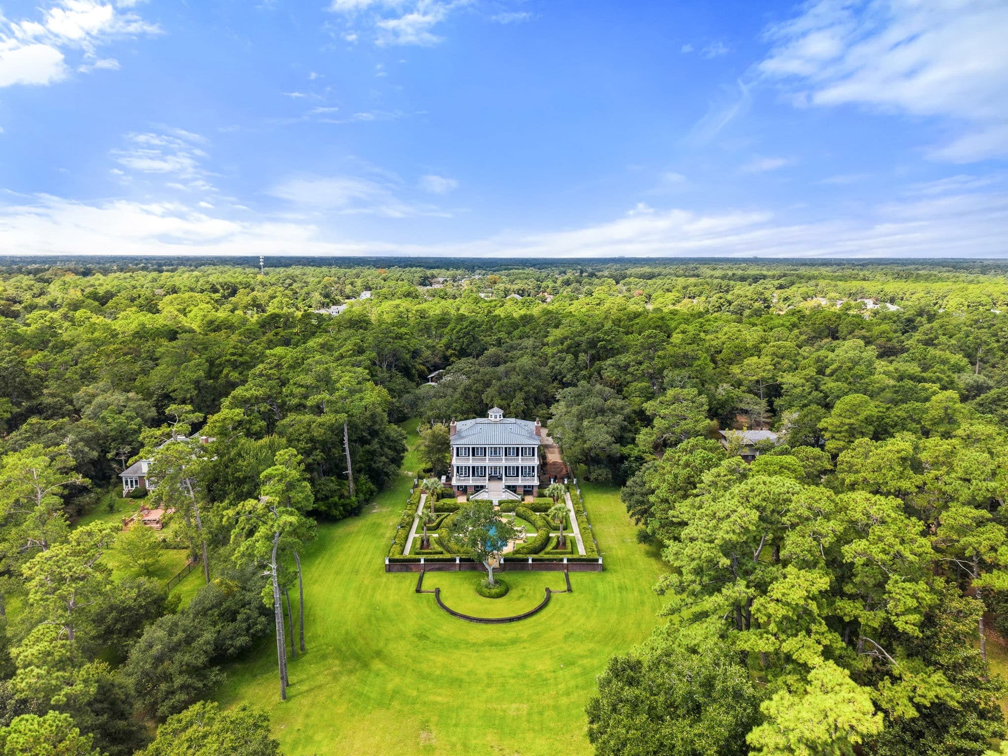 Aerial view of a long lawn approach lined with trees leading to the house and its walled entrance garden.