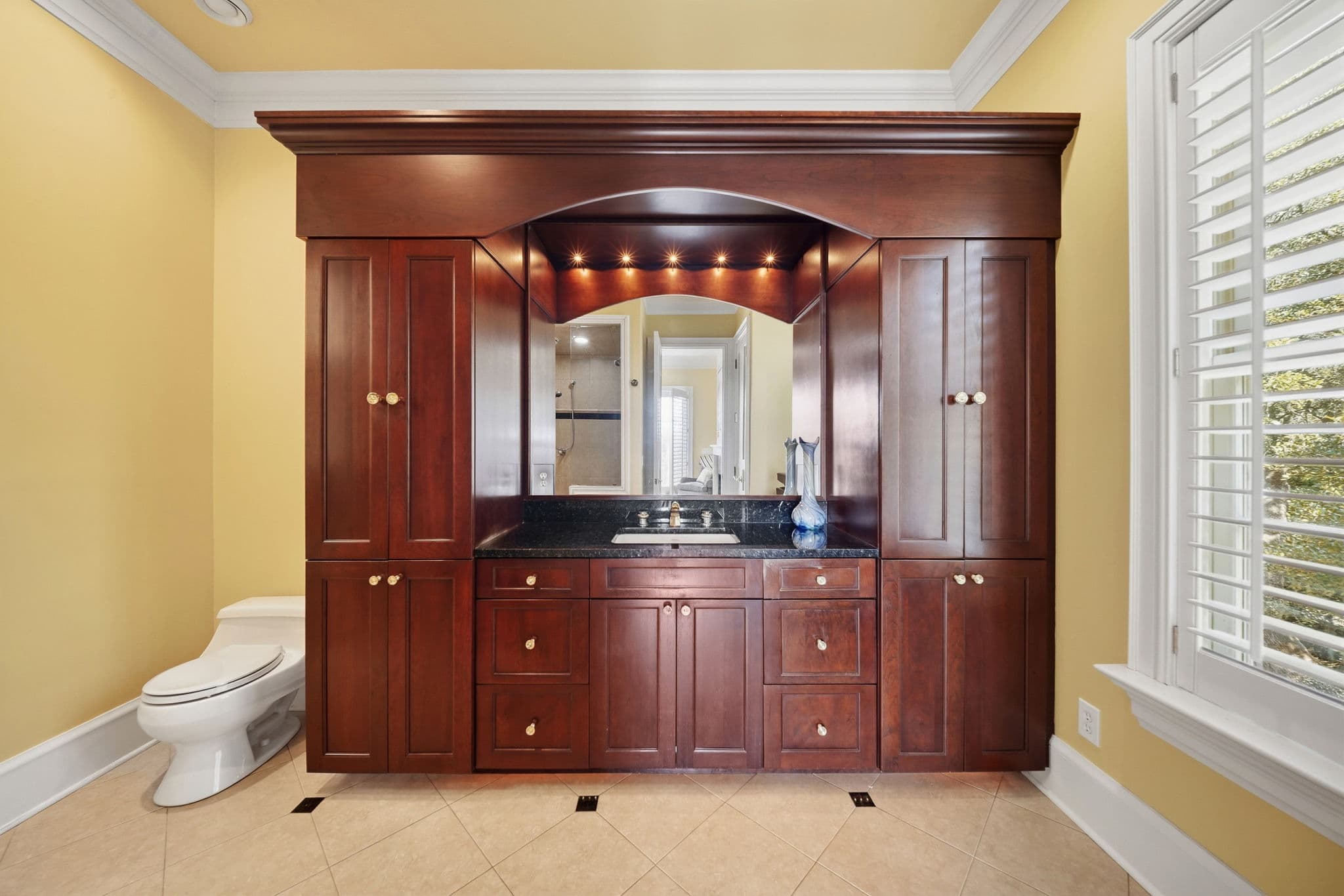 Bathroom vanity in dark wood with a black granite counter, a large mirror, and an overhead lighting niche.